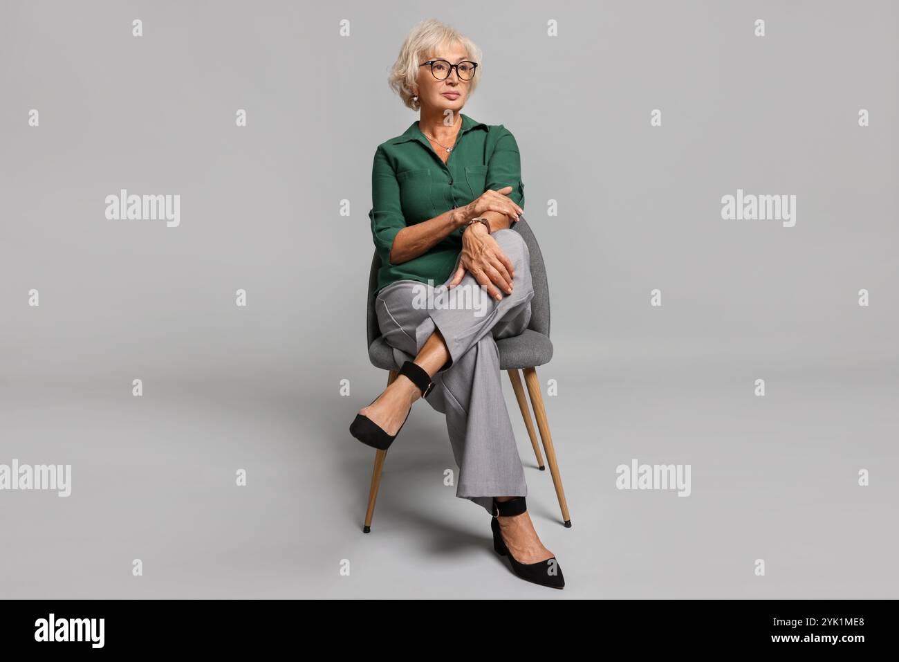Beautiful senior woman sitting on chair against light grey background ...