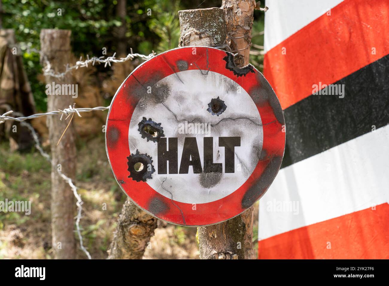 Stop Sign In German On A Bullet riddled Sign On A Barbed Wire Fence 