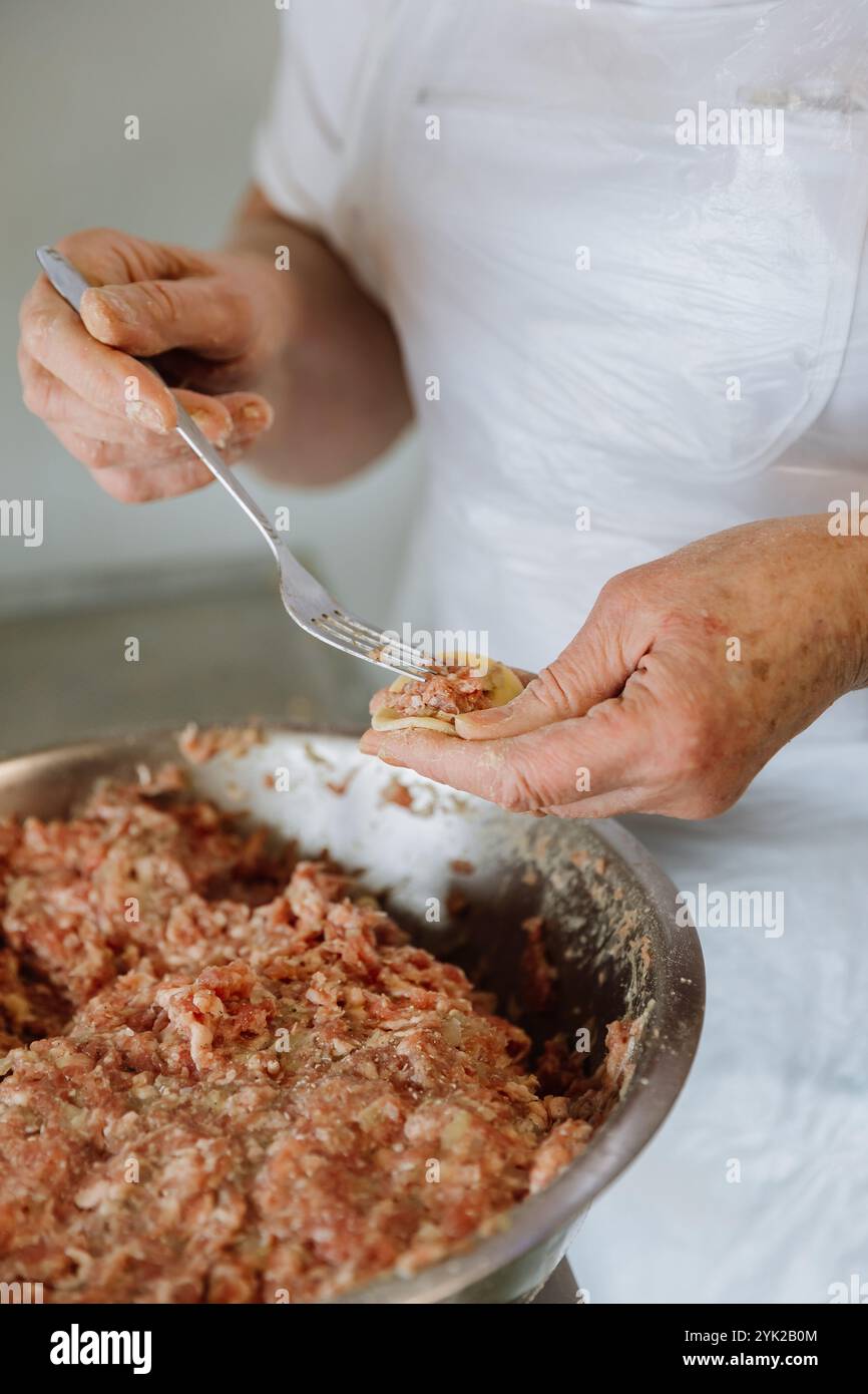 Filling a handmade dumpling with minced meat using a fork, traditional cooking process close up Stock Photo