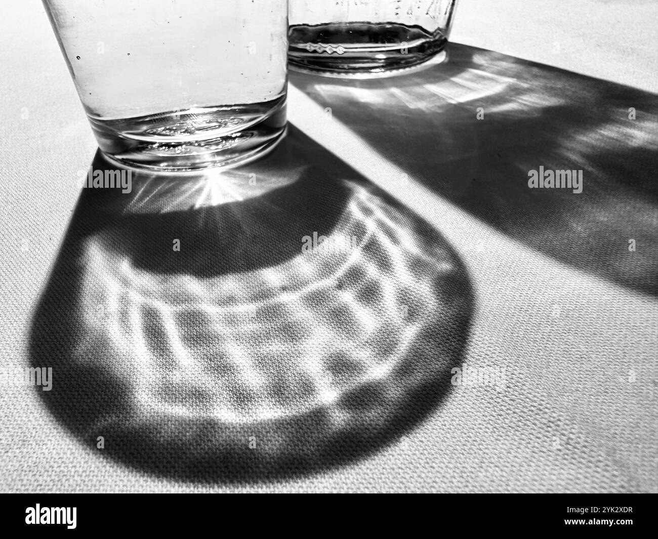 A glass of water and a water bottle and their shadows on a white table cloth - Smartphone Captured Stock Image