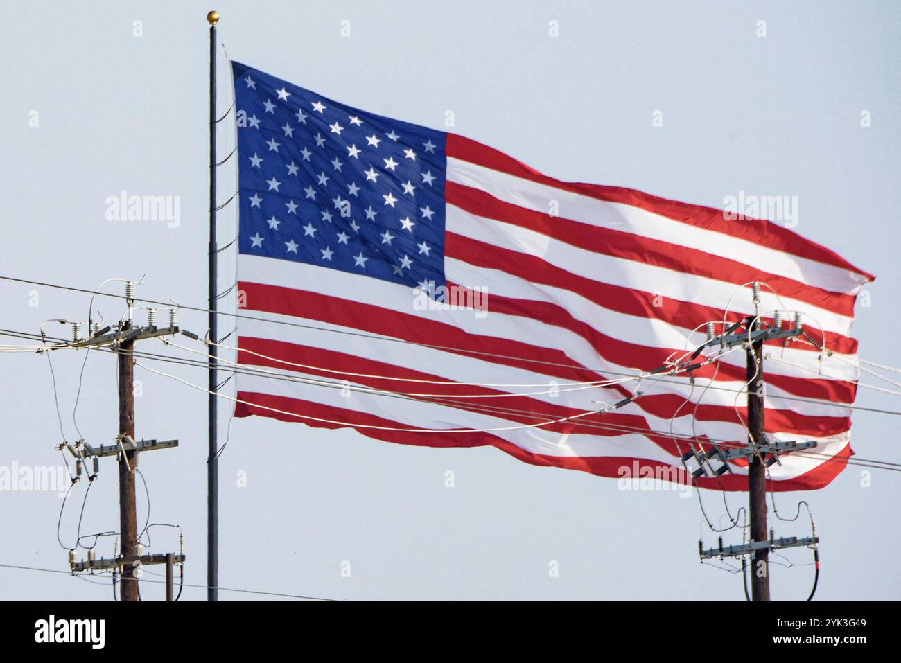 US Flag waving in the wind (a safe distance) behind electrical power poles, in Bexar County, Texas, on June 5, 2024.  Providing reliable, affordable electricity is essential to sustaining the economic well-being and quality of life for all of the nation's rural residents.  The U/S. Department of Agriculture (USDA) Rural Development (RD) Rural Utilities Service (RUS) Electric Program provides leadership and capital to maintain, expand, upgrade, and modernize America's vast rural electric infrastructure. Stock Photo