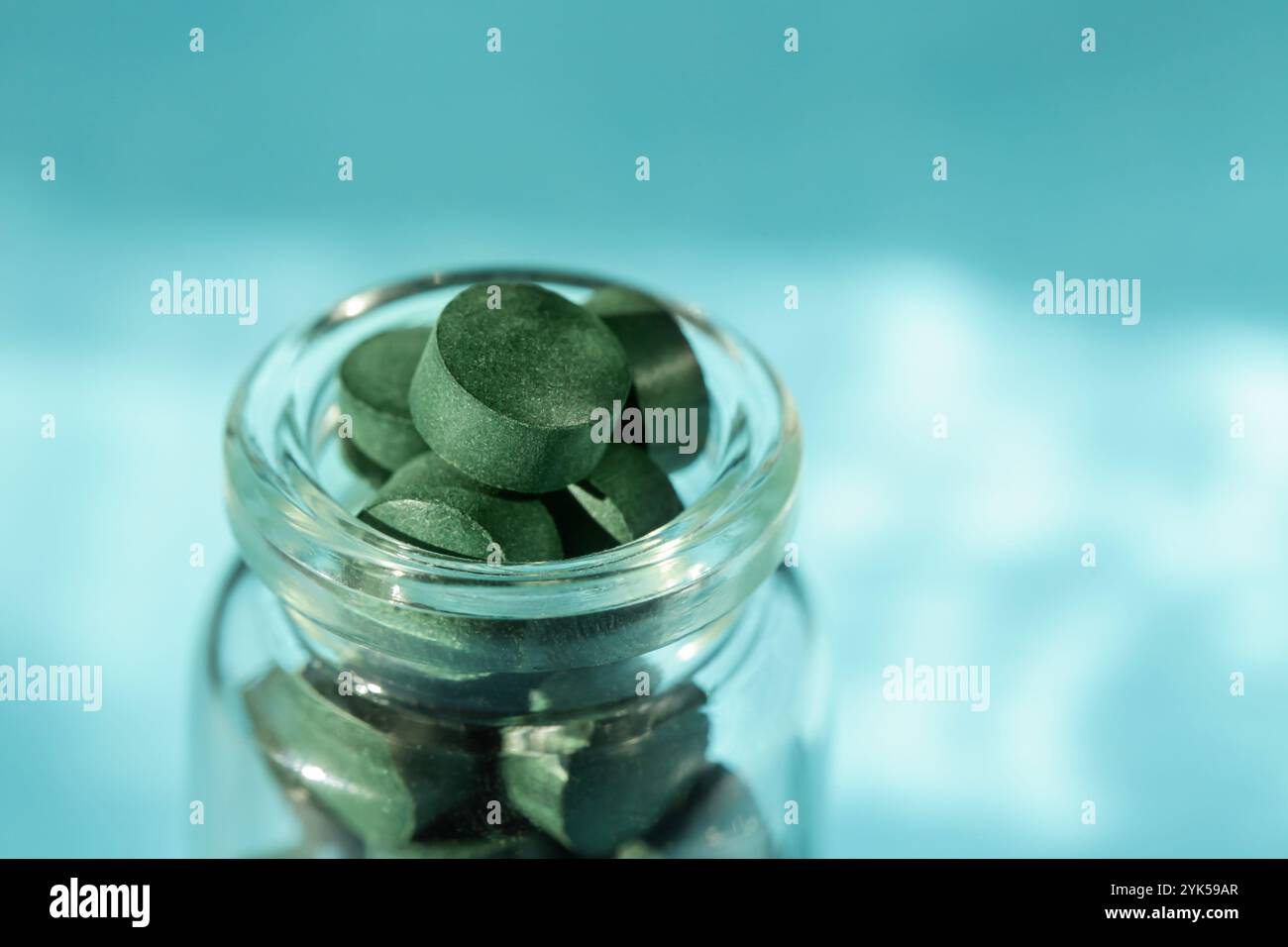 Spirulina pills in glass bottle on blue background. Antioxidant nutrition. Copy space Stock Photo