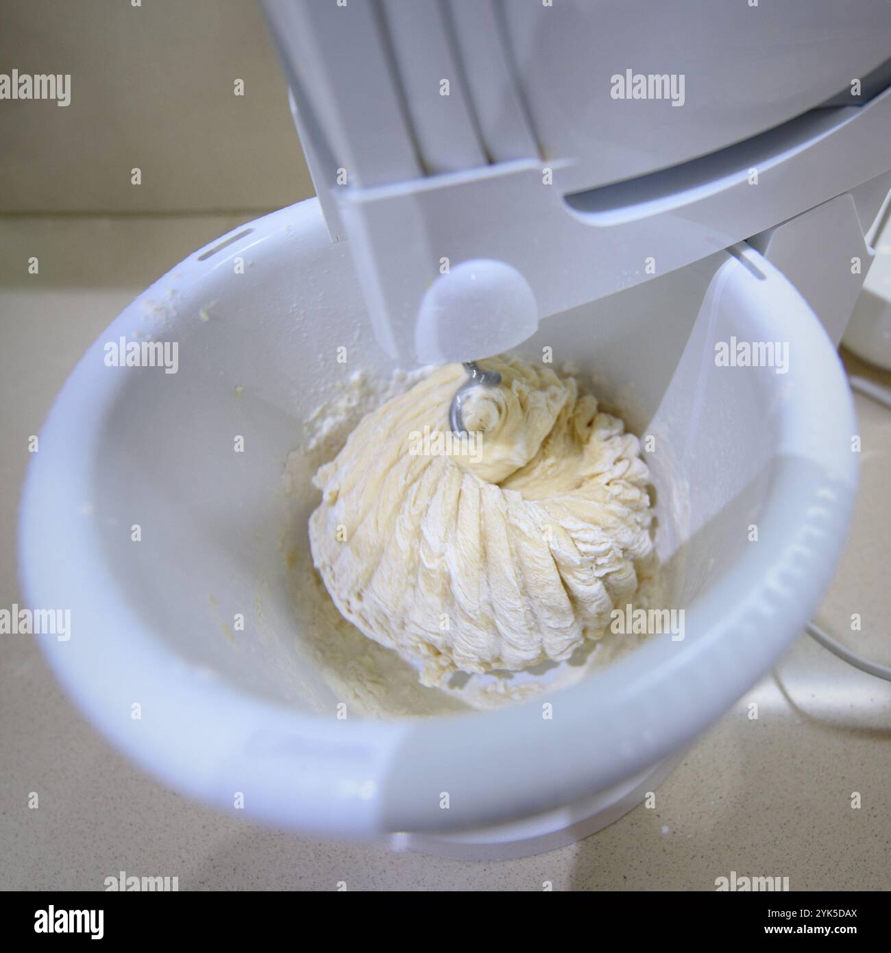 Using an electric mixer to whip together cake batter in a white bowl on a kitchen countertop. Stock Photo