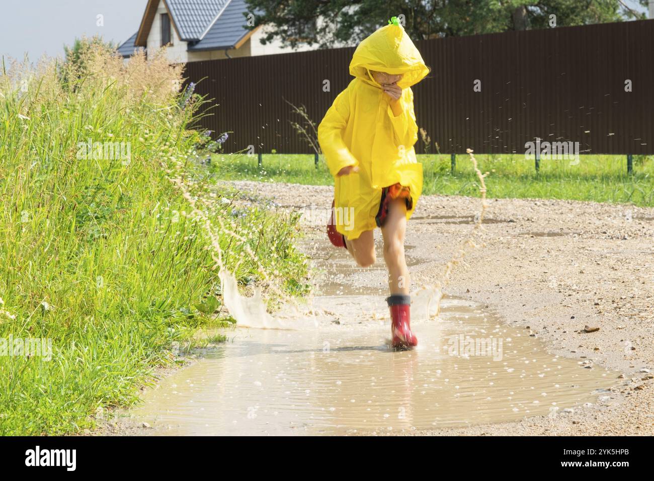 A girl in red rubber boots and a yellow raincoat runs through puddles ...