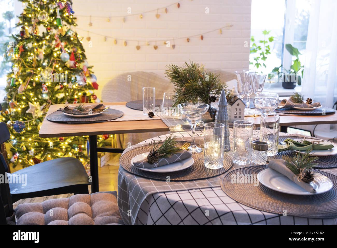 Serving a festive table with plates, forks, knives, napkins, glasses close-up in the modern interior of a loft house decorated for Christmas and New Y Stock Photo