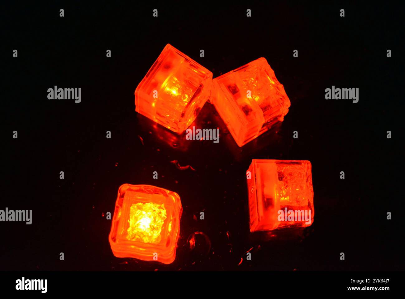Red glowing ice cubes are located on a black glossy with water drops ...