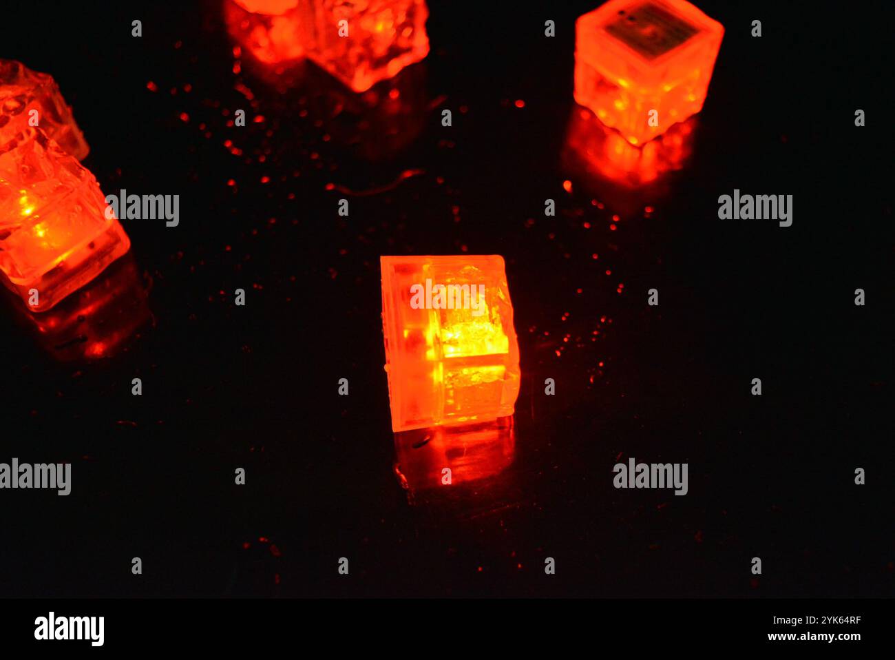 Red glowing ice cubes are located on a black glossy with water drops ...