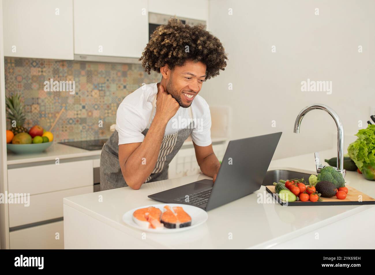 Young man prepares sushi while using laptop in modern kitchen Stock Photo