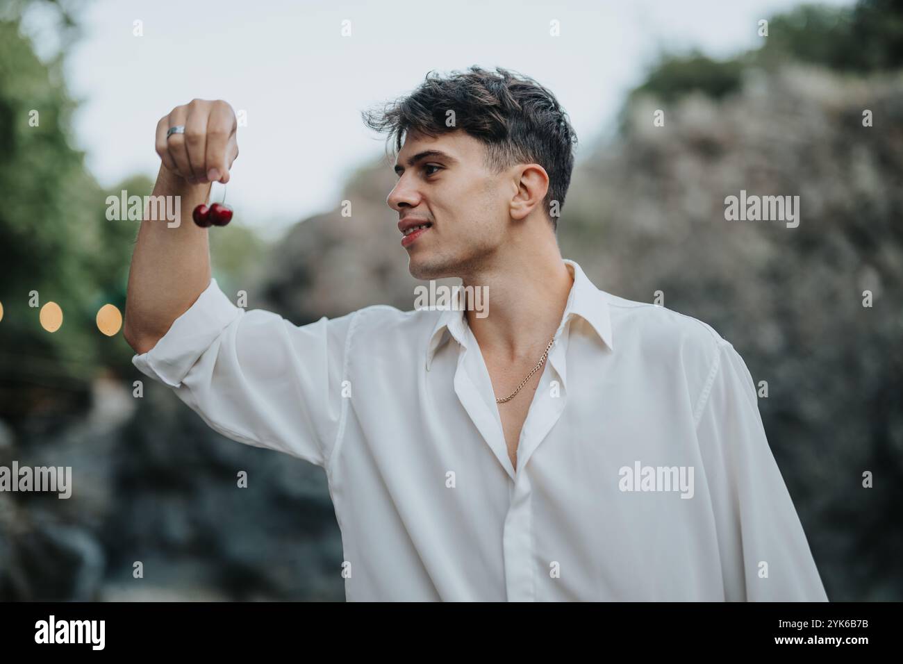 Man smiling and holding cherries outdoors in a relaxed setting Stock Photo