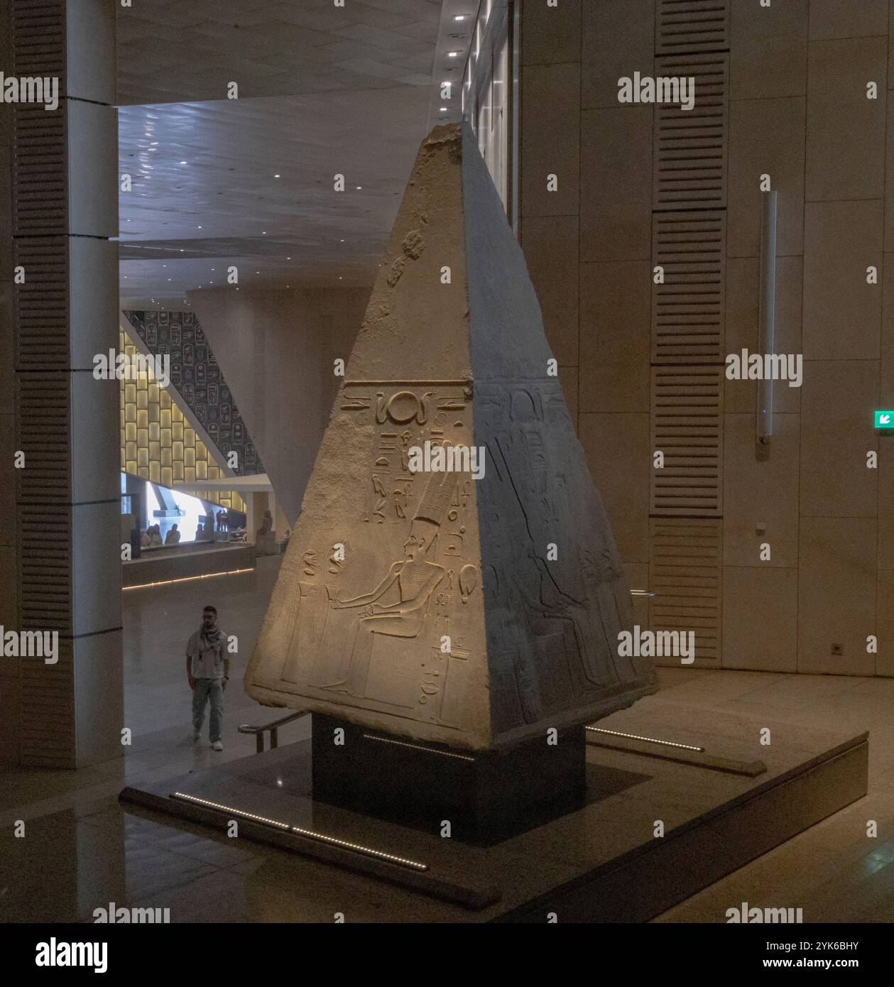 A visitor is dwarfed by a monumental exhibit just off the Grand Staircase in the Grand Egyptian Museum (GEM). Stock Photo