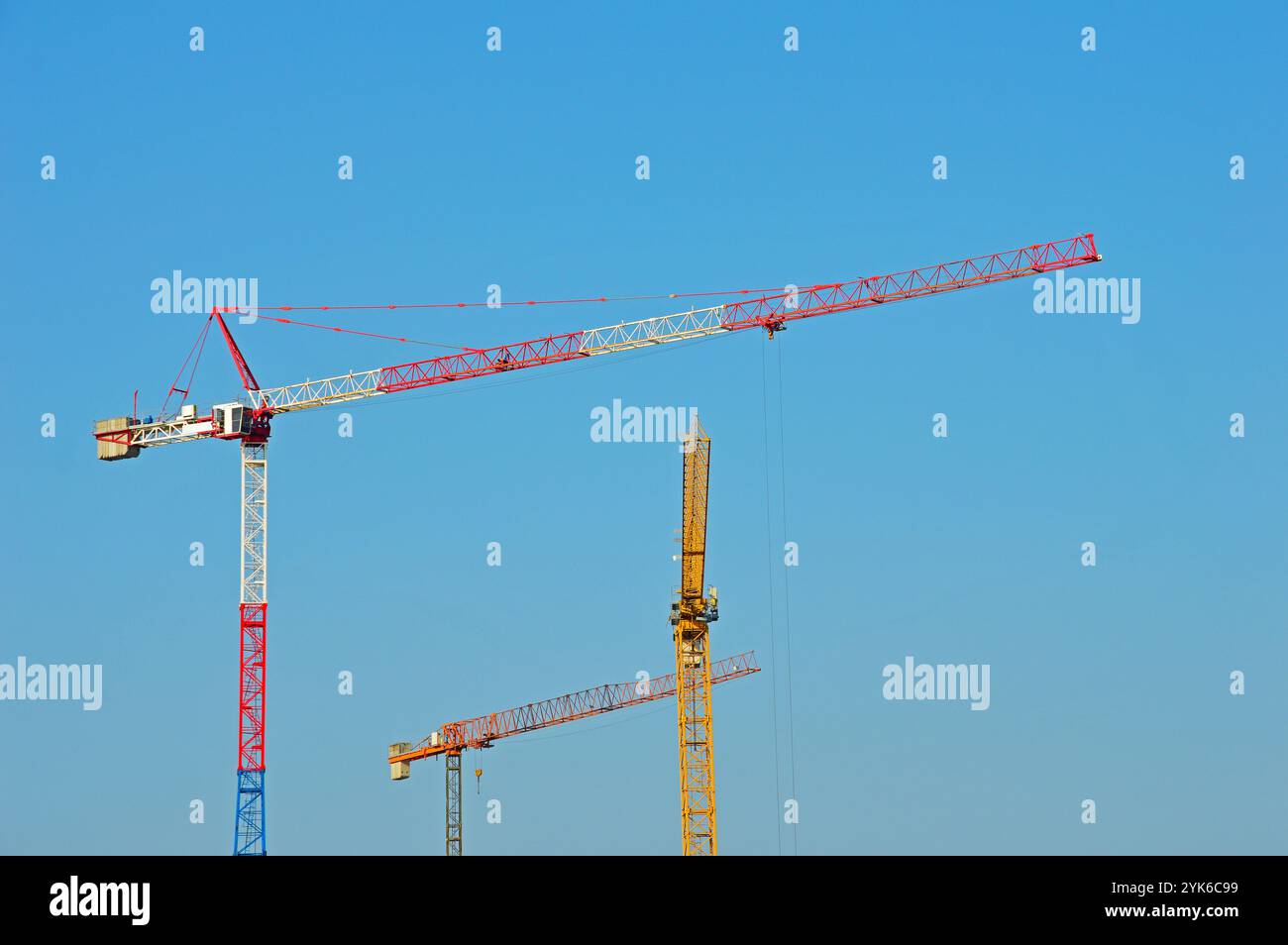 Three multi-colored tower cranes against a cloudless sky Stock Photo