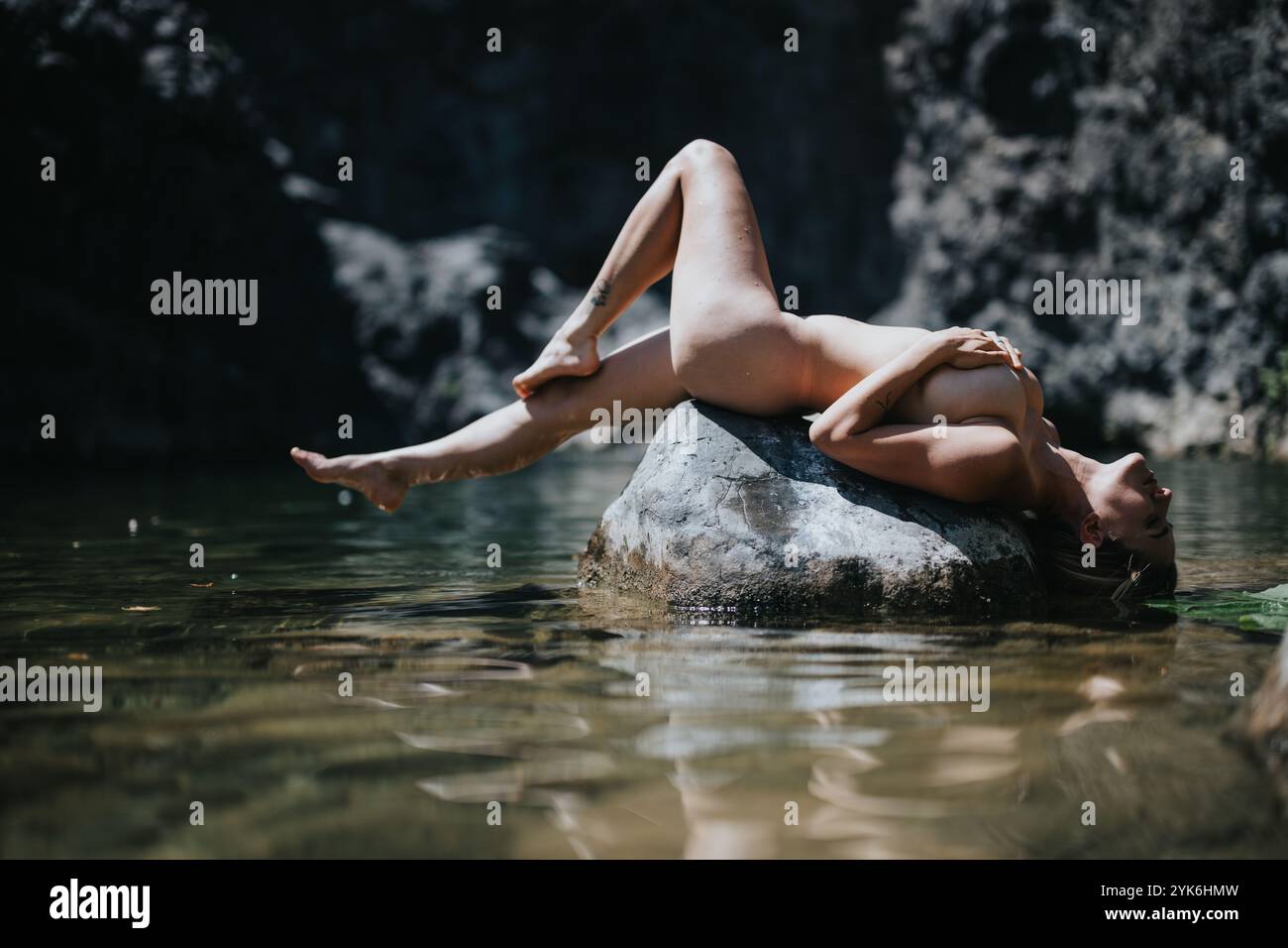 Serene woman lying on rock in tranquil water surrounded by natural landscape, basking in sunlight and relaxation Stock Photo