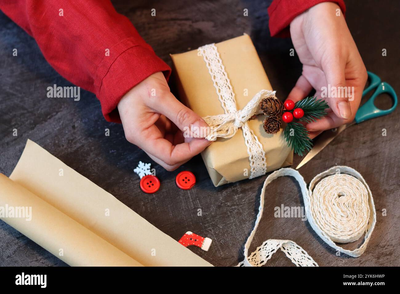 Hands of a girl in a red dress decorating a gift box with lace ribbon. Female hands holding a gift box. Stock Photo