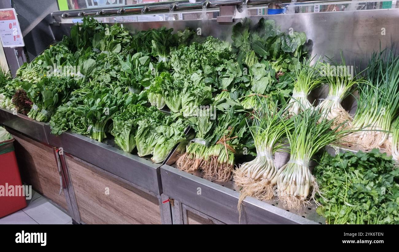A vibrant display of fresh leafy greens at a supermarket in China. The stand showcases a variety of vegetables, including lettuce and scallions. - Smartphone Captured Stock Image