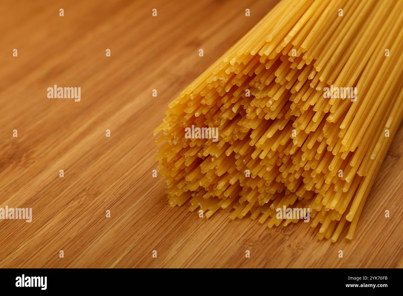 Bundle of uncooked dry spaghetti tied with string, resting on a wooden cutting board, ready for cooking and italian cuisine preparation, high angle vi Stock Photo