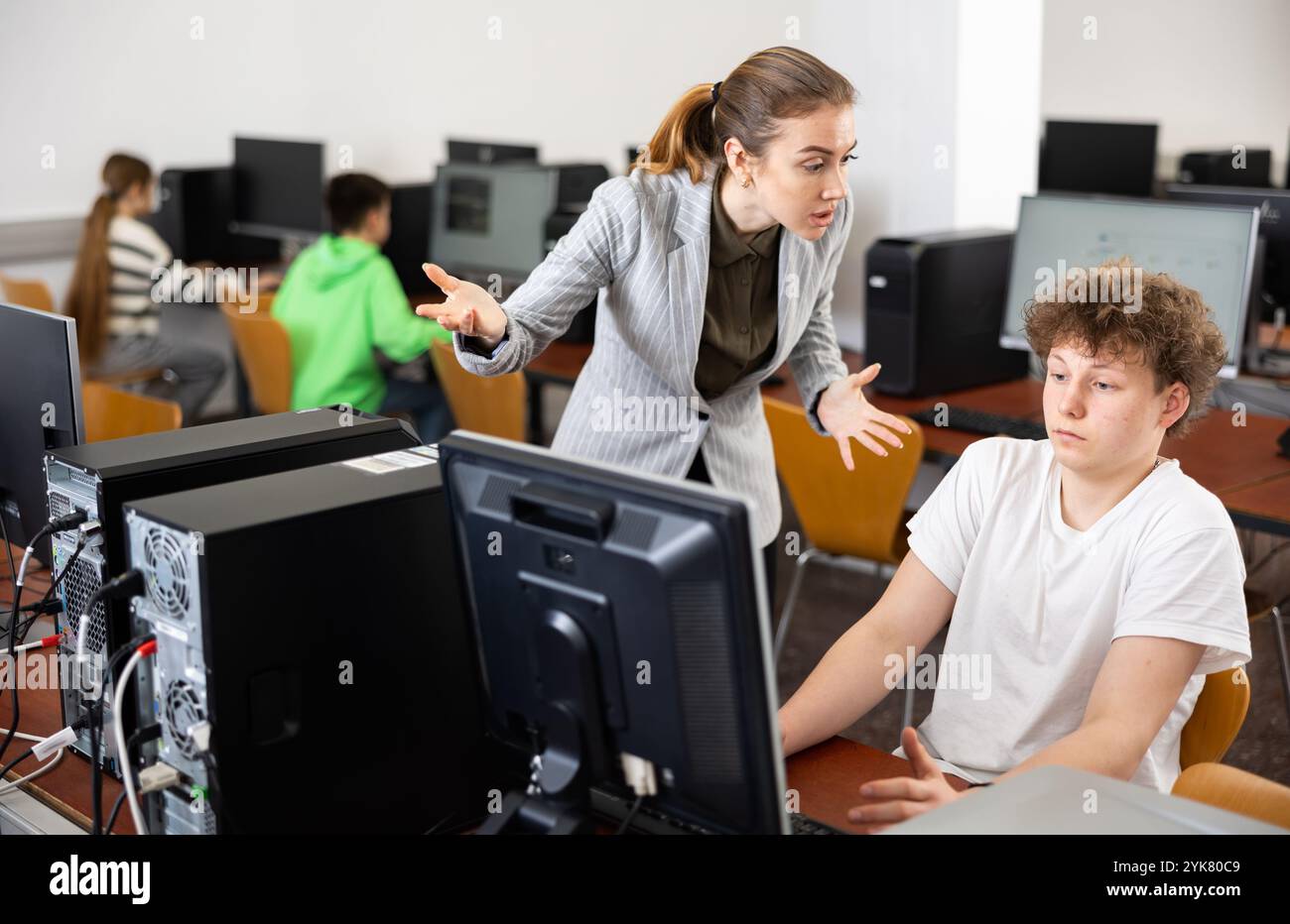 Strict teacher reprimanding negligent teenage student in computer class Stock Photo