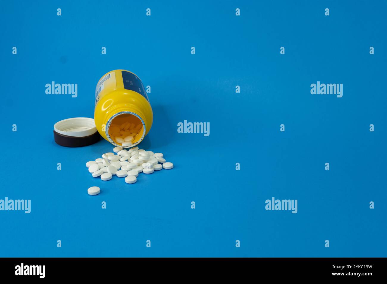 Regular Aspirin has been spilled out over a Blue Background. The drug container is lying on its side, open. Stock Photo