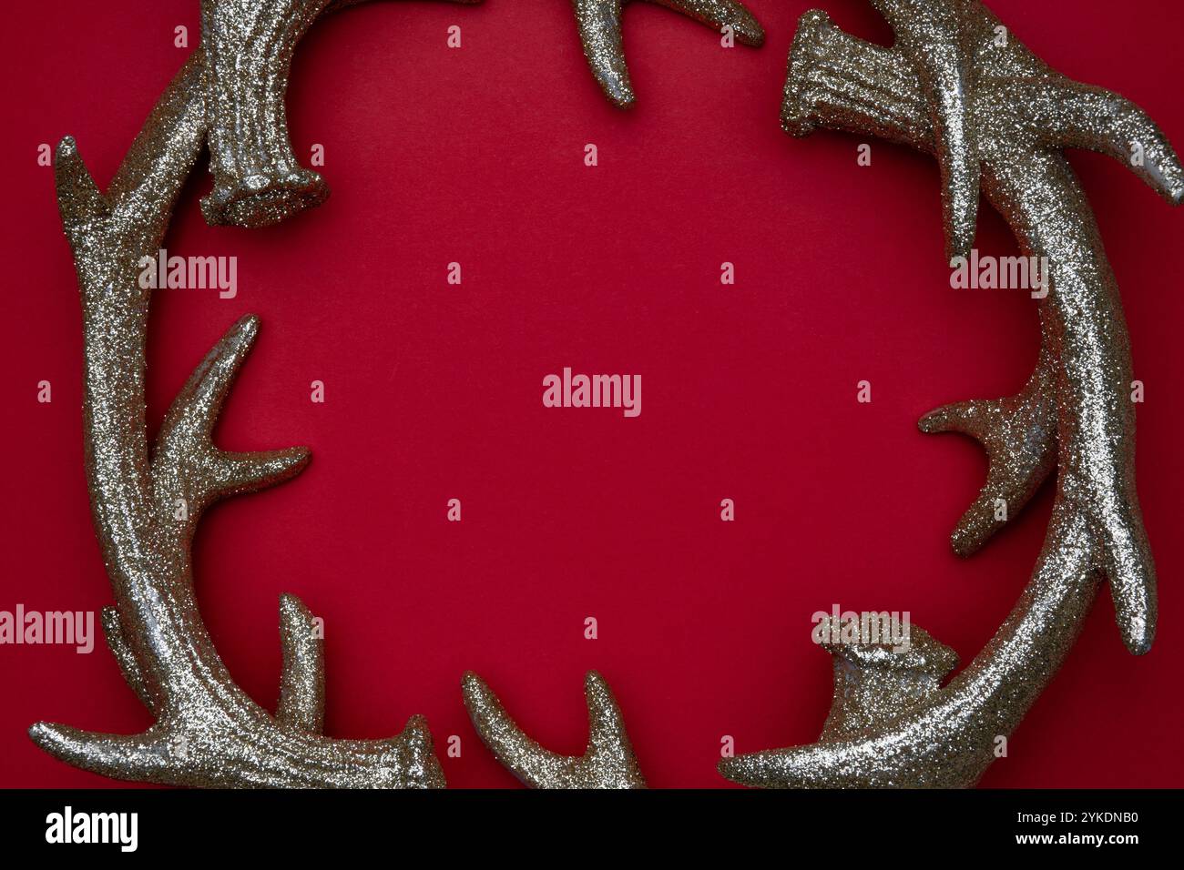 A decorative golden antler wreath is showcased on a vibrant red backdrop, adding a festive touch to holiday arrangements. Stock Photo