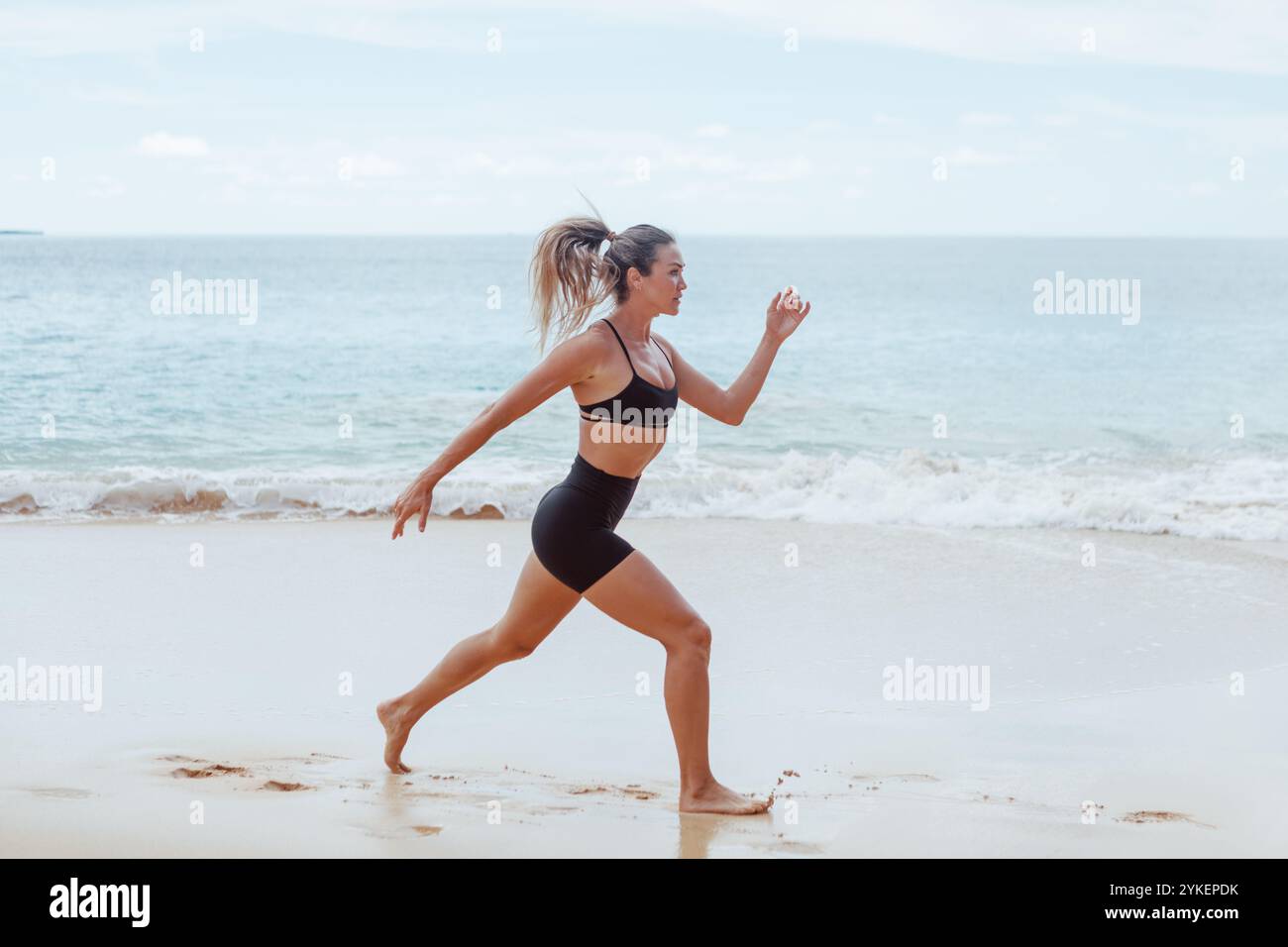 Woman doing jump squats on beach Stock Photo