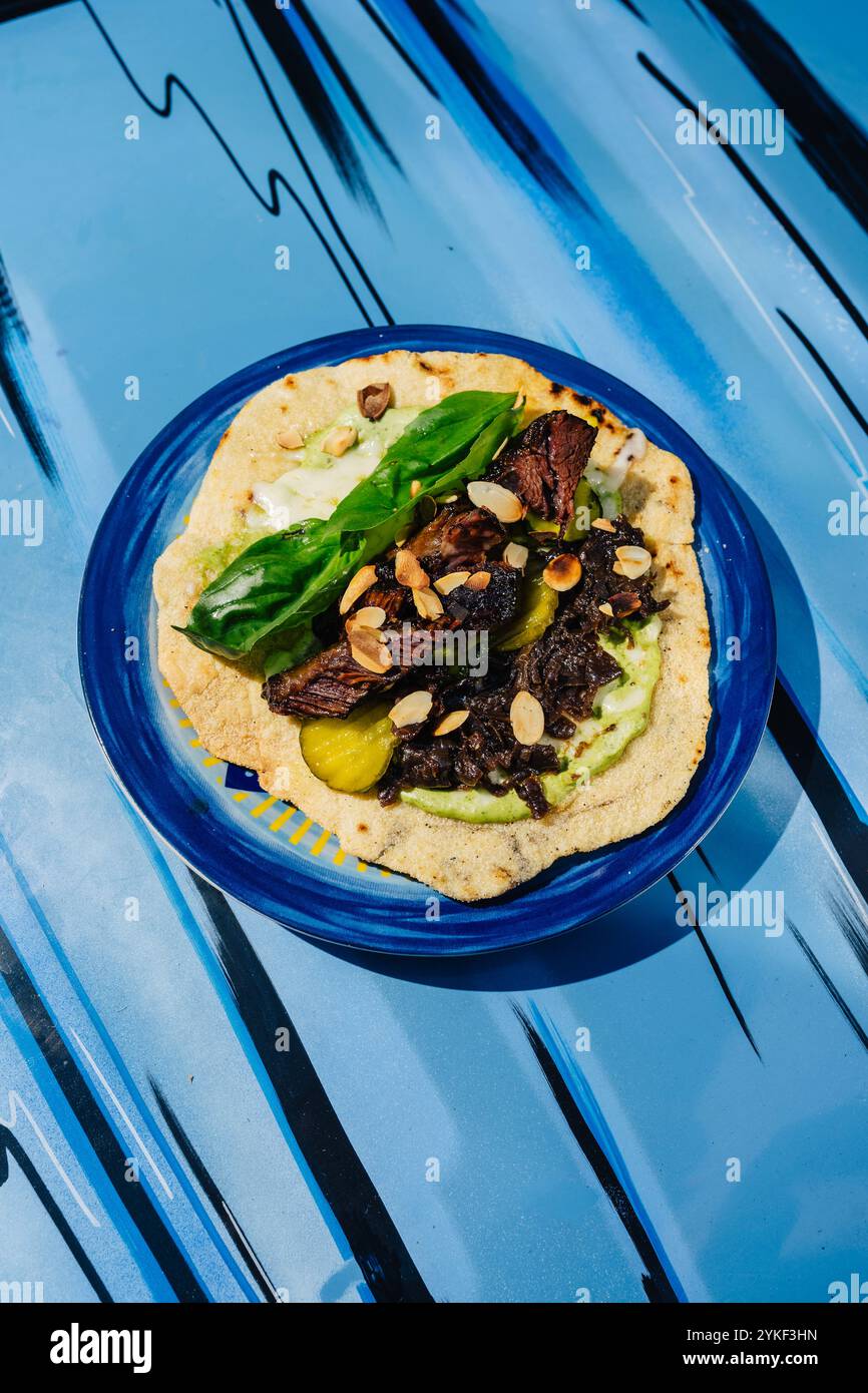 A gourmet presentation of veal cheeks tortilla garnished with almonds and fresh basil on a vibrant blue plate, enhancing its visual appeal. Stock Photo