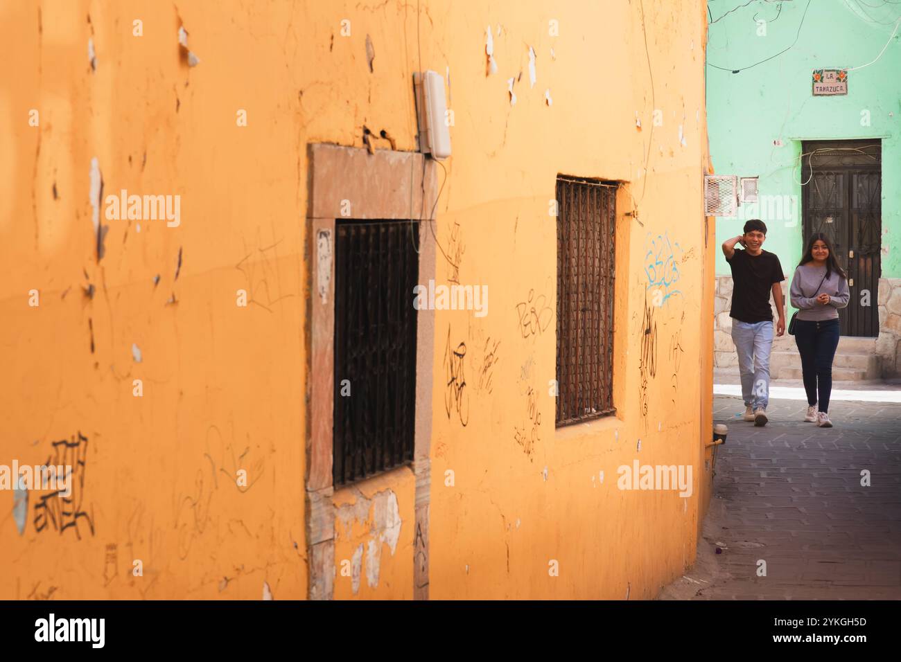 Guanajuato, Mexico - February 6, 2024: A young couple strolls along a textured, colorful wall in Guanajuato, Mexico, capturing a casual moment in the Stock Photo