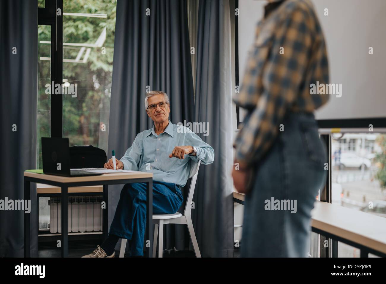 Elderly professor engaging with students in a modern classroom Stock Photo