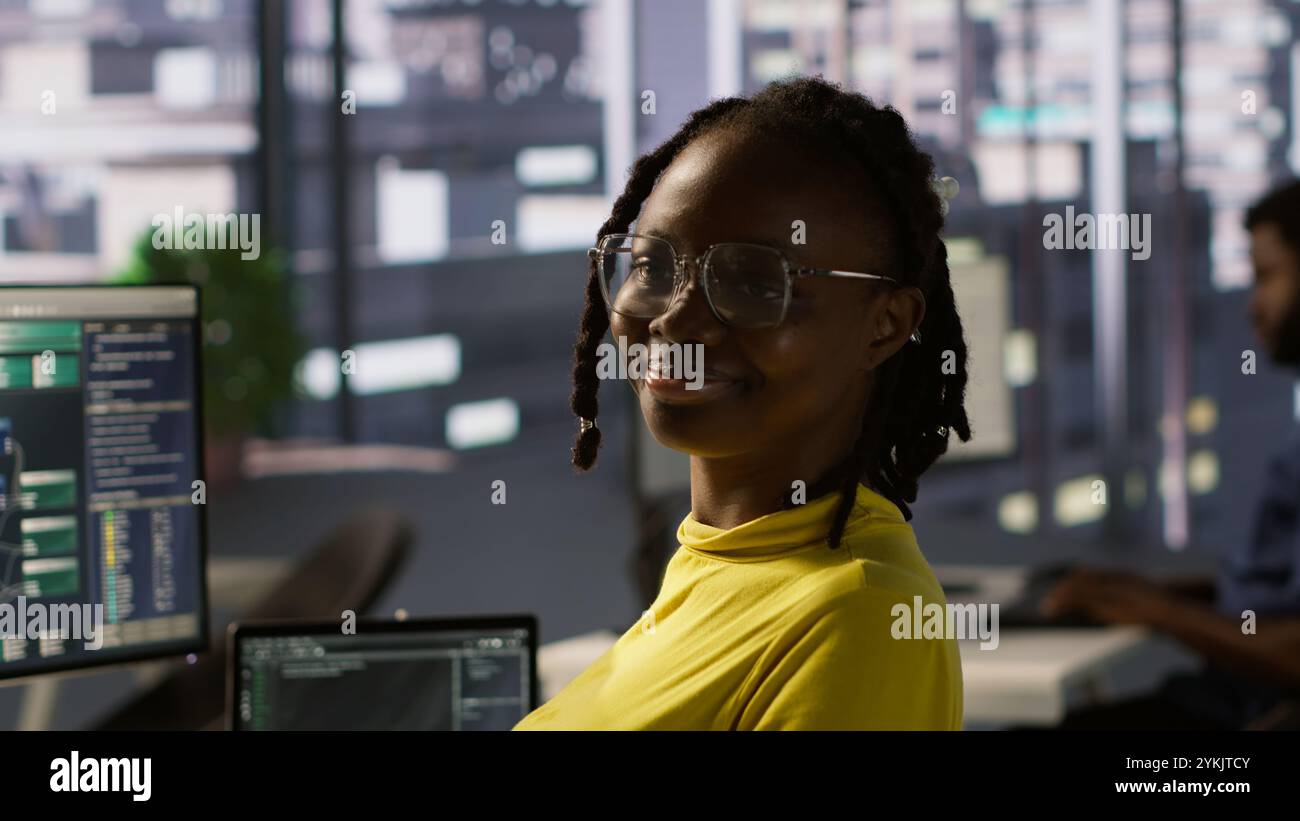 Portrait of smiling computer scientist at work doing software debugging using PC, checking glitches in lines of code. Cheerful IT specialist in office fixing coding issues using computer, camera A Stock Photo