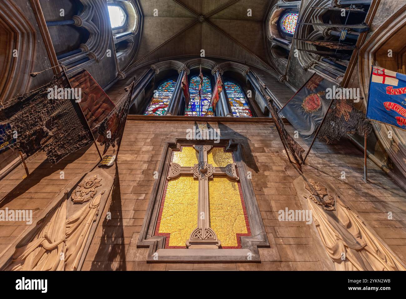 The Chancel of St. Patrick's Cathedral in Dublin features a large mosaic cross, flanked by military regimental flags and stone carvings. Above, the go Stock Photo