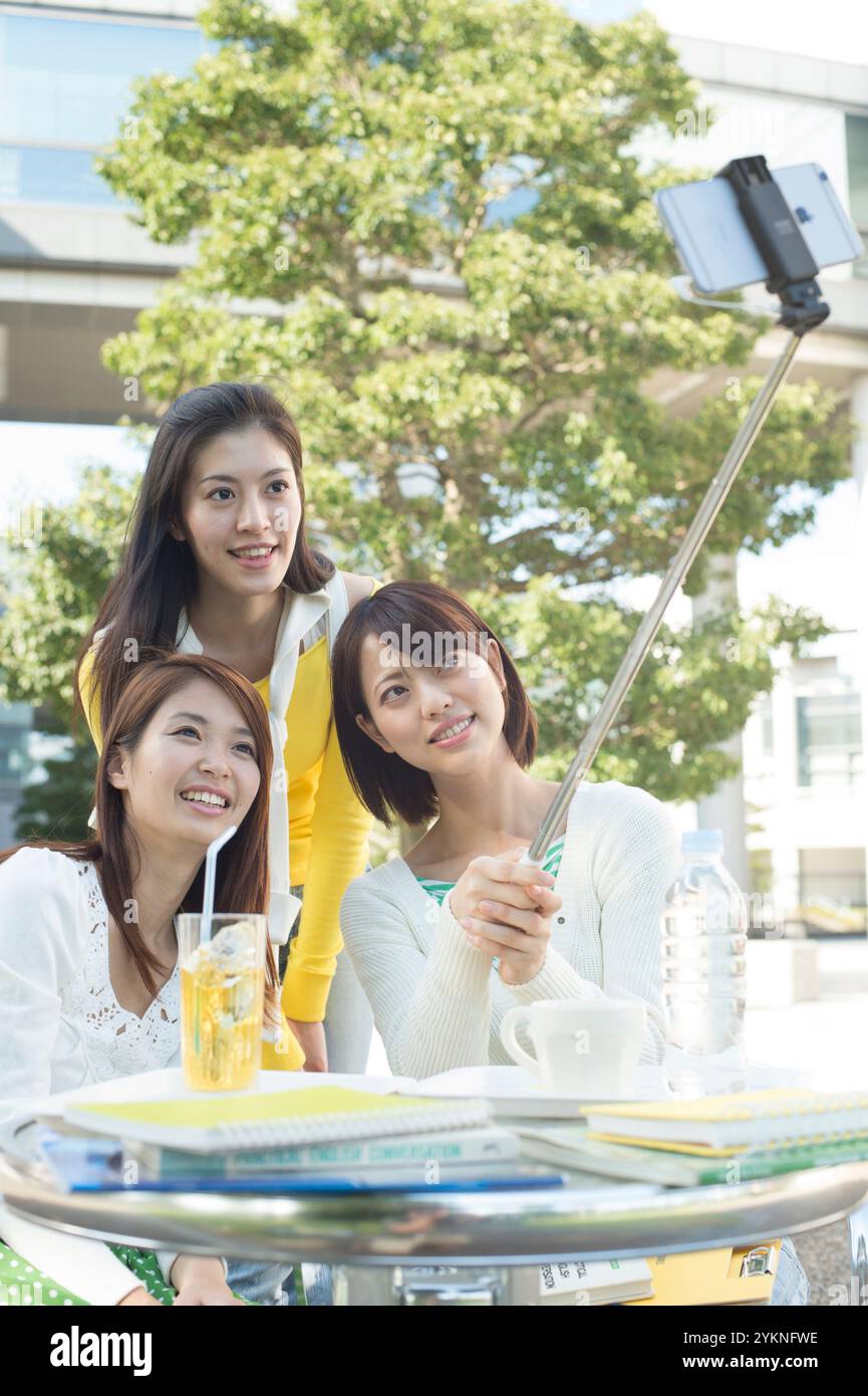 Three female university students taking selfie stick photos in campus cafeteria Stock Photo
