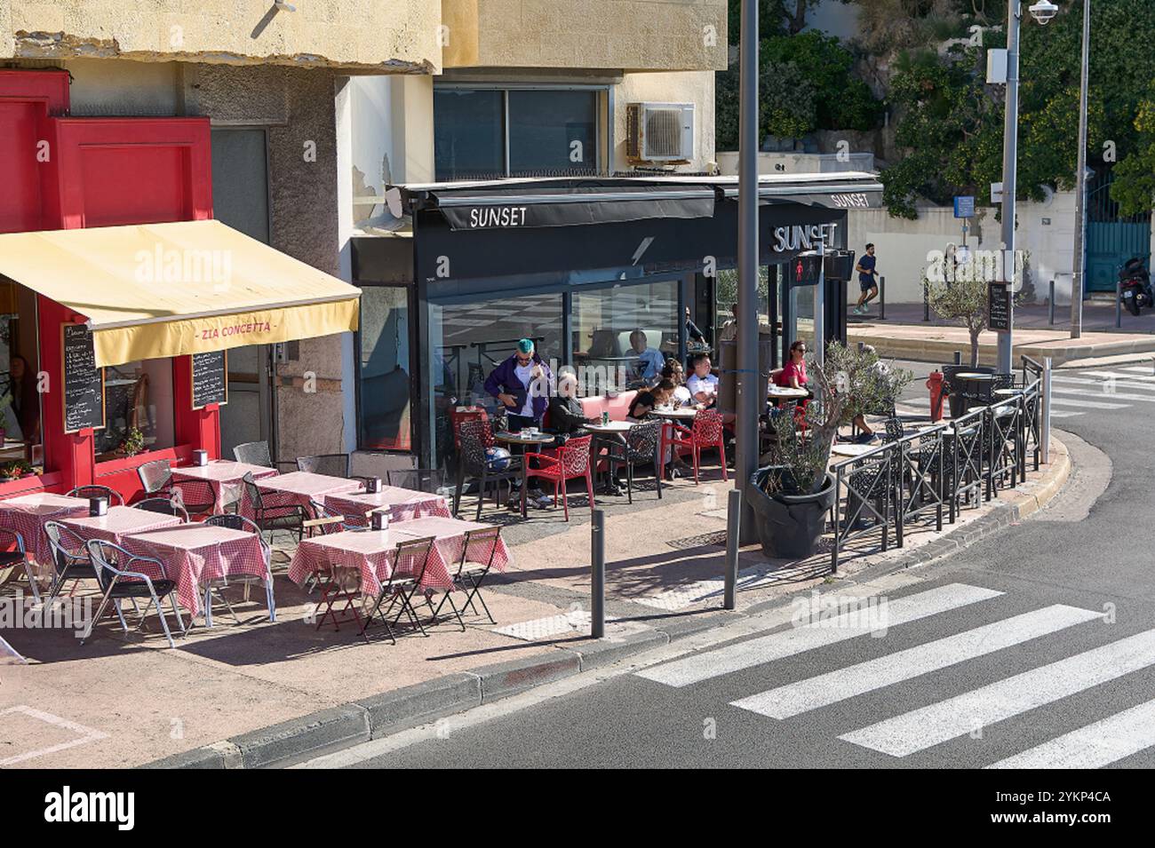 Viladecans. Spain - November 19,2024: Outdoor caf on a sunny corner in Marseille, with red and white tables and chairs, and customers enjoying drinks Stock Photo