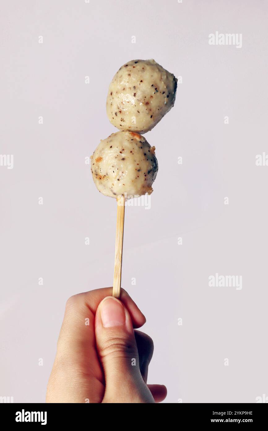 Japanese oden black pepper fish ball, chicken meatball, isolated white meatball delicious yummy. Hand holding fish ball on stick seafood street food Stock Photo