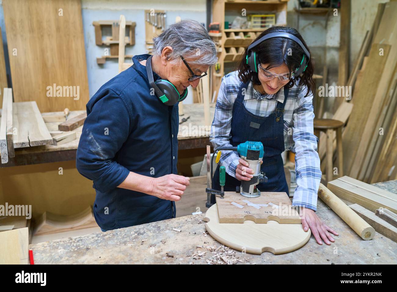 An experienced craftsman mentors a young apprentice in a lumberyard, focusing on woodworking skills and teamwork. This showcases professional training Stock Photo