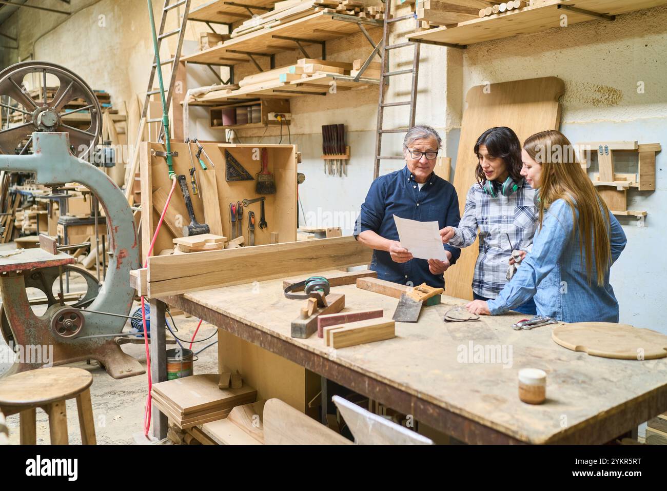 A diverse group of people in a lumberyard collaborating on a woodworking project, emphasizing teamwork, learning, and hands-on skills. The scene captu Stock Photo