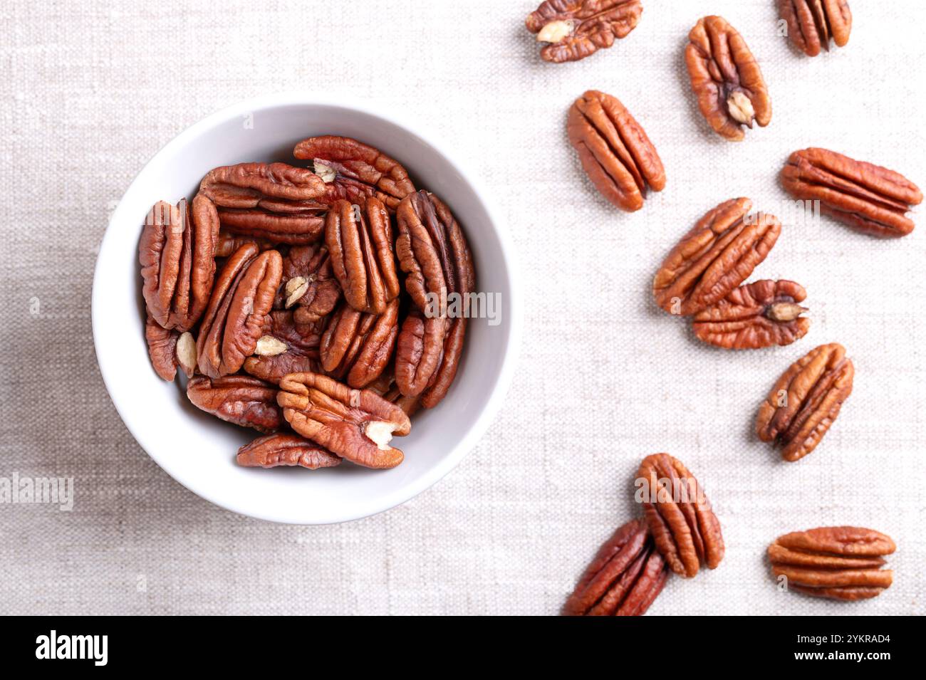 Pecan halves in a white bowl on linen fabric. Shelled and dried pecan nuts, seeds and fruits of Carya illinoinensis. Stock Photo