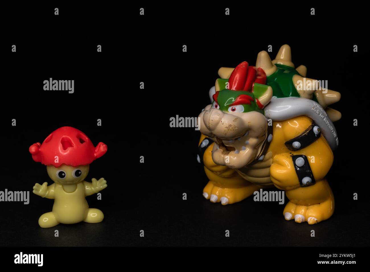 Two plastic figure toys standing on a black background. Mushroom-like figurine from Kinder Surprise with King Bowser character from Super Mario. Stock Photo