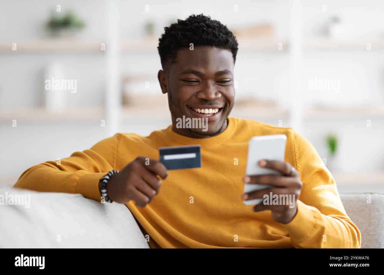 Positive black man using cellphone and credit card at home Stock Photo