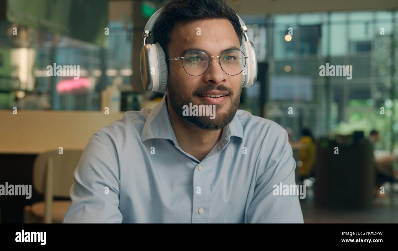 Indian ethnic guy male businessman freelancer visitor cafe drink coffee break smiling business man listen music headphones drinking tea in restaurant Stock Photo