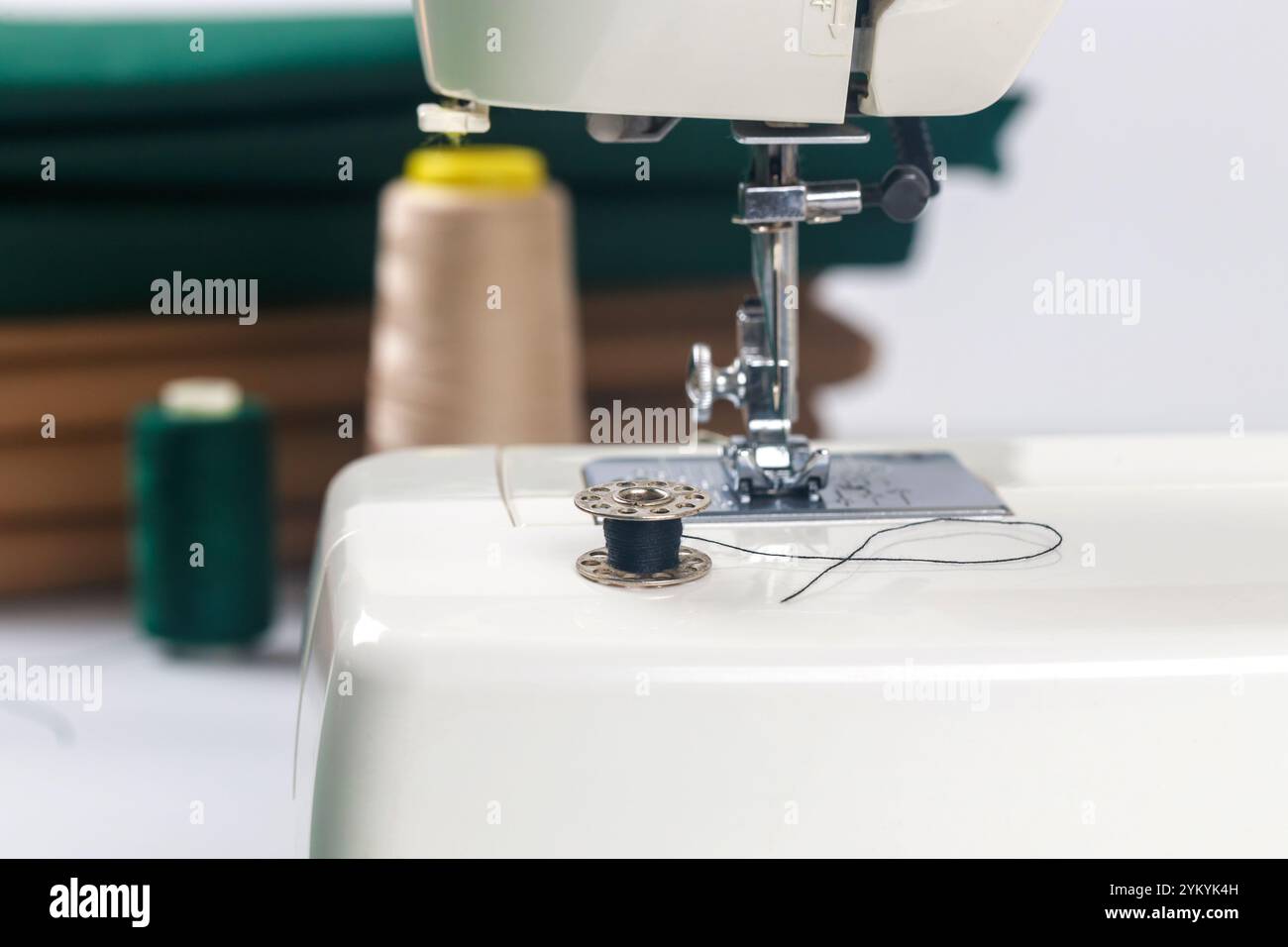 Sewing machine with black thread and spools on table in crafting space during daylight Stock Photo