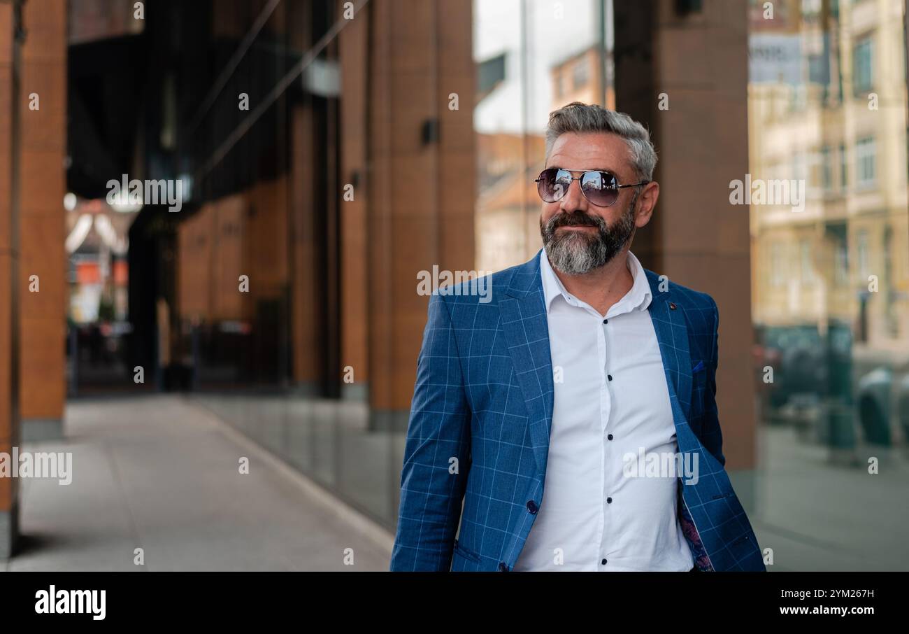 A handsome mature business man is walking through the city street near the office building. Stock Photo