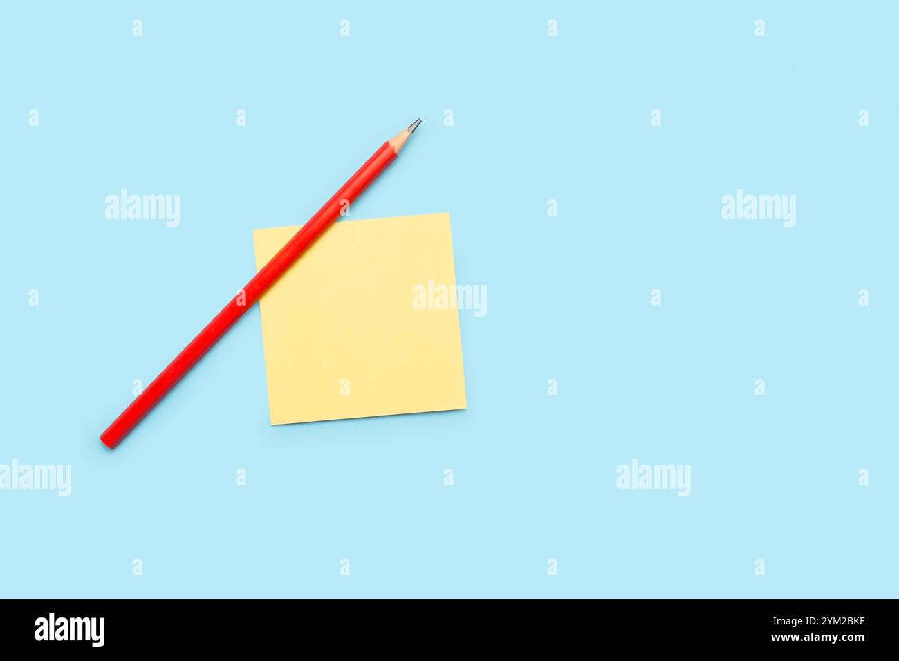 A pencil and a yellow paper note on a light blue background Stock Photo
