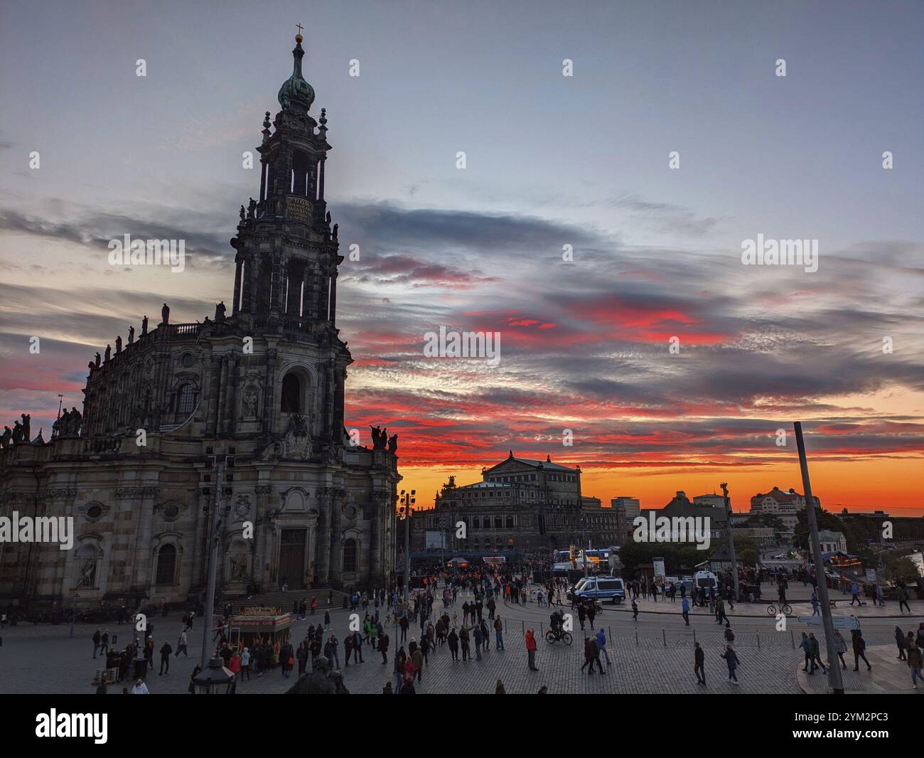 A bustling plaza with dramatic sunset and silhouettes of buildings ...
