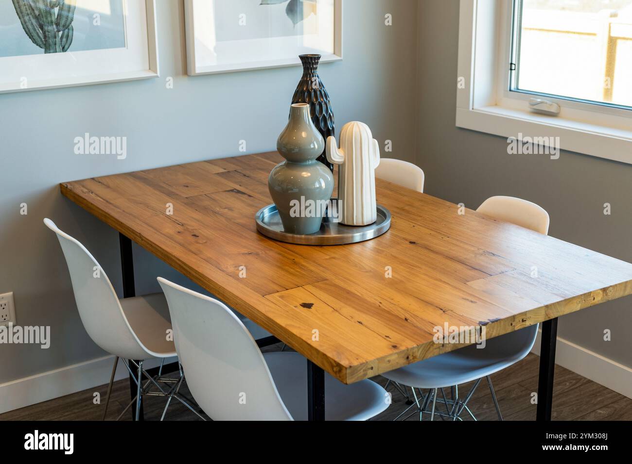 A wooden dining table with four white chairs around it. A vase with a ...