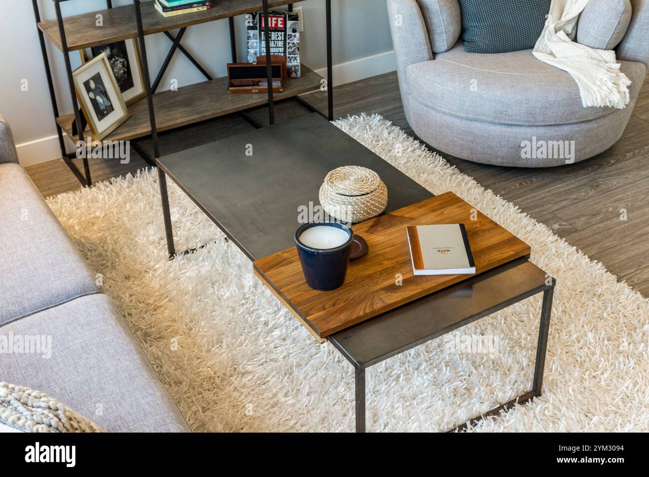 A living room with a coffee table and a chair. The coffee table has a book and a cup on it Stock Photo