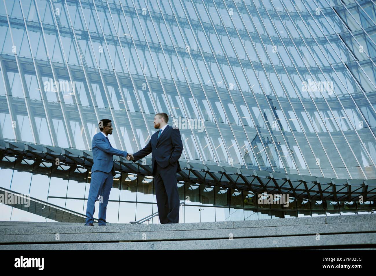 Two businessmen shaking hands in modern glass building with reflections ...