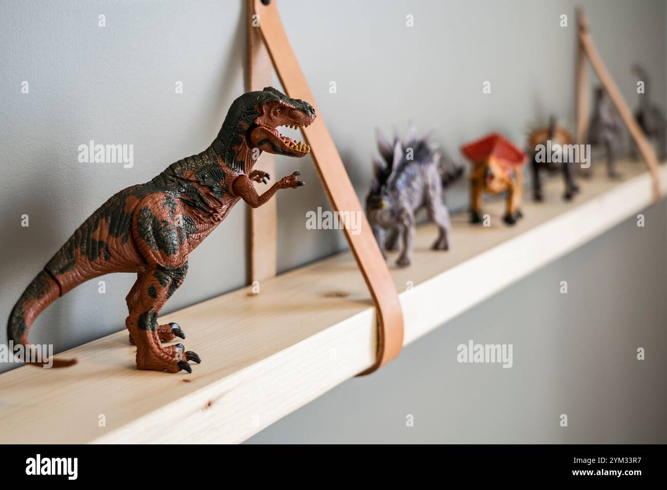A dinosaur toy is on a shelf with other dinosaur toys. The shelf is ...