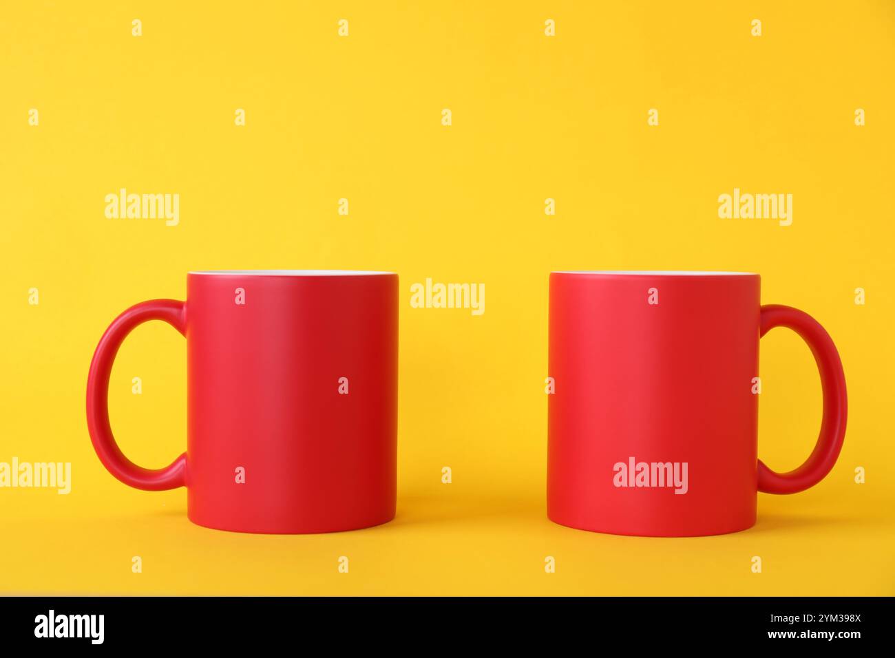 Two blank red mugs on yellow background. Mockup for design Stock Photo
