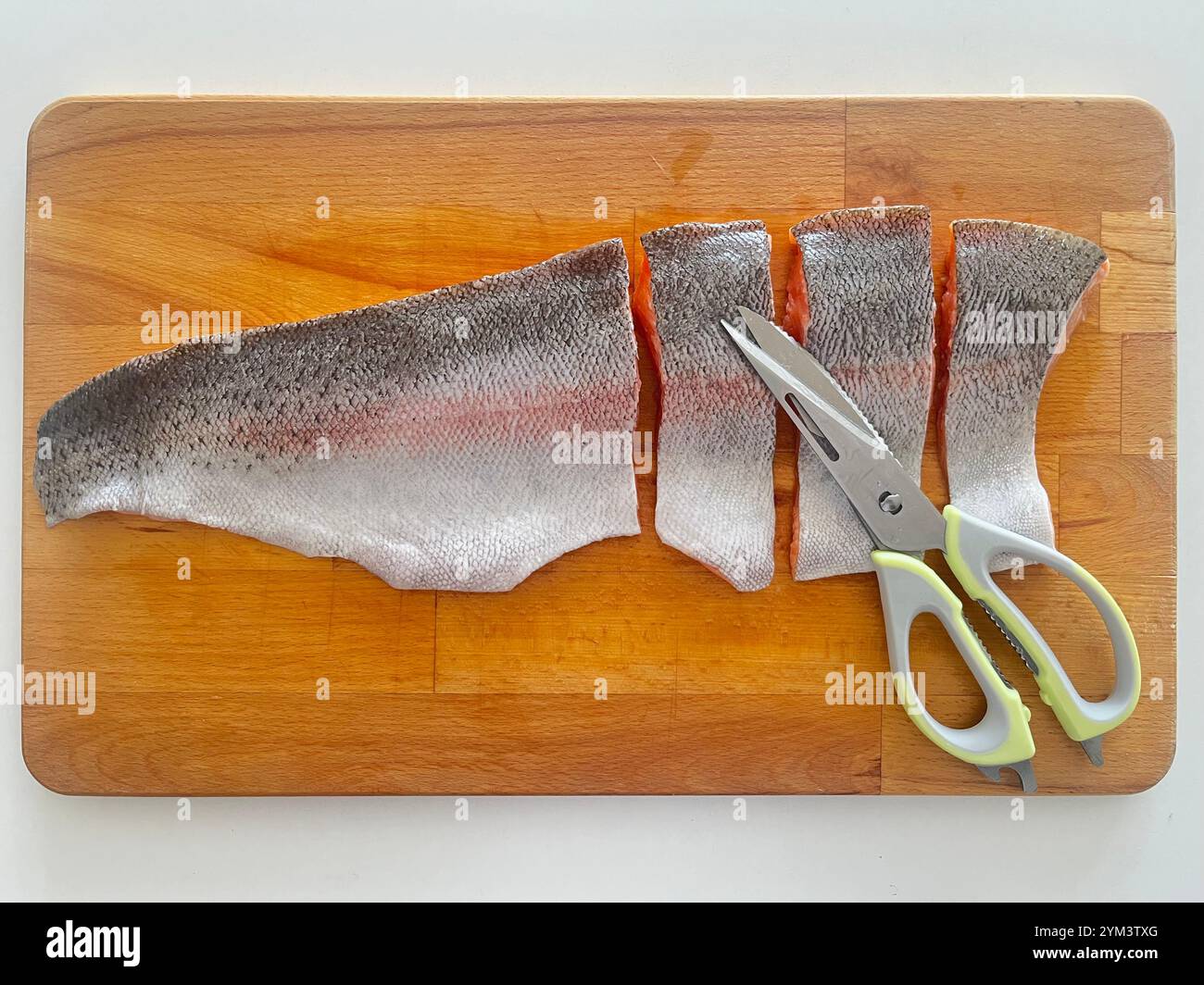 Cut raw Sea Trout fish fillet and scissors on wooden cutting board, home fish cooking preparations. - Smartphone Captured Stock Image