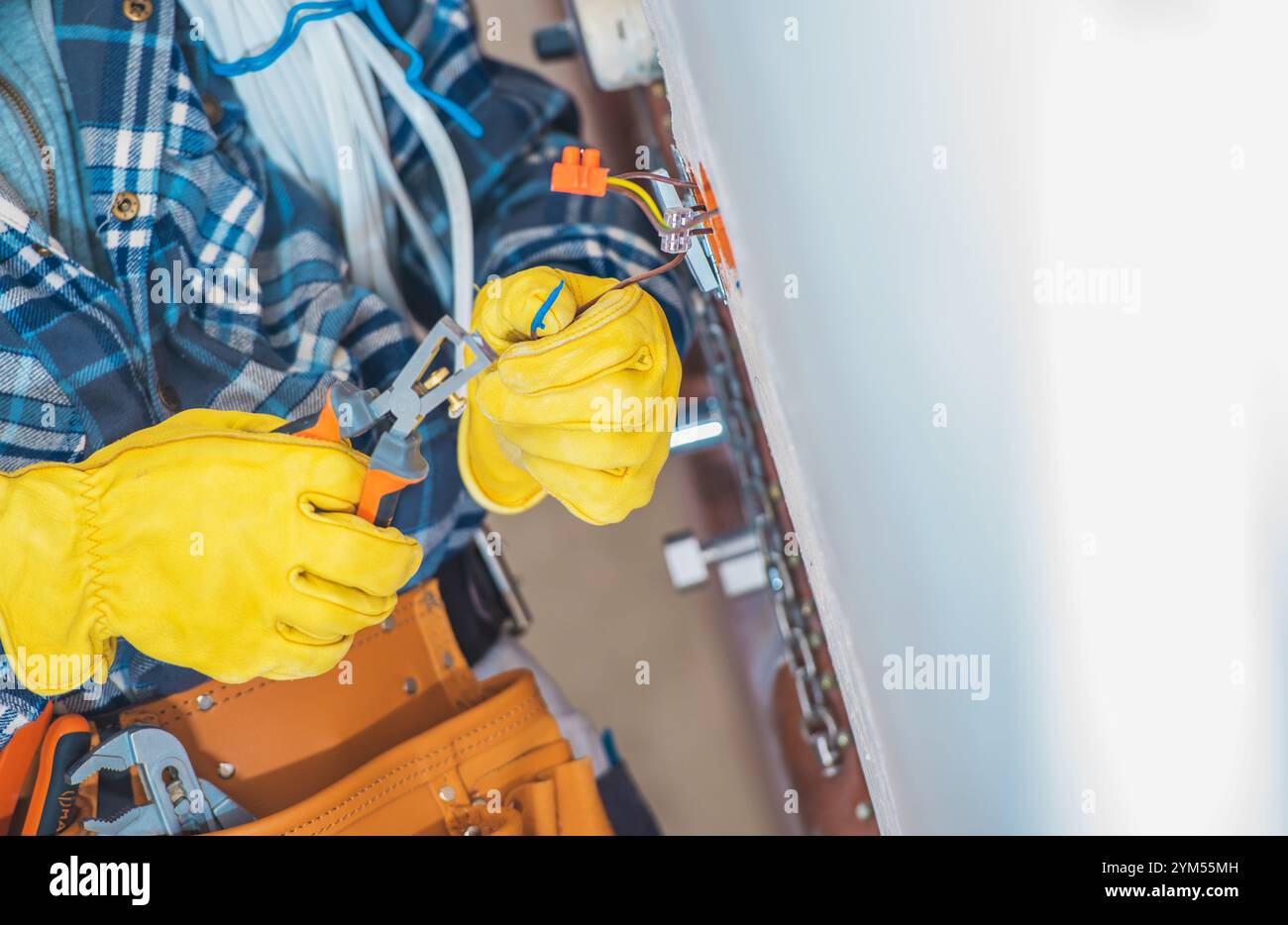 An electrician in yellow gloves uses tools to work on electrical wiring ...