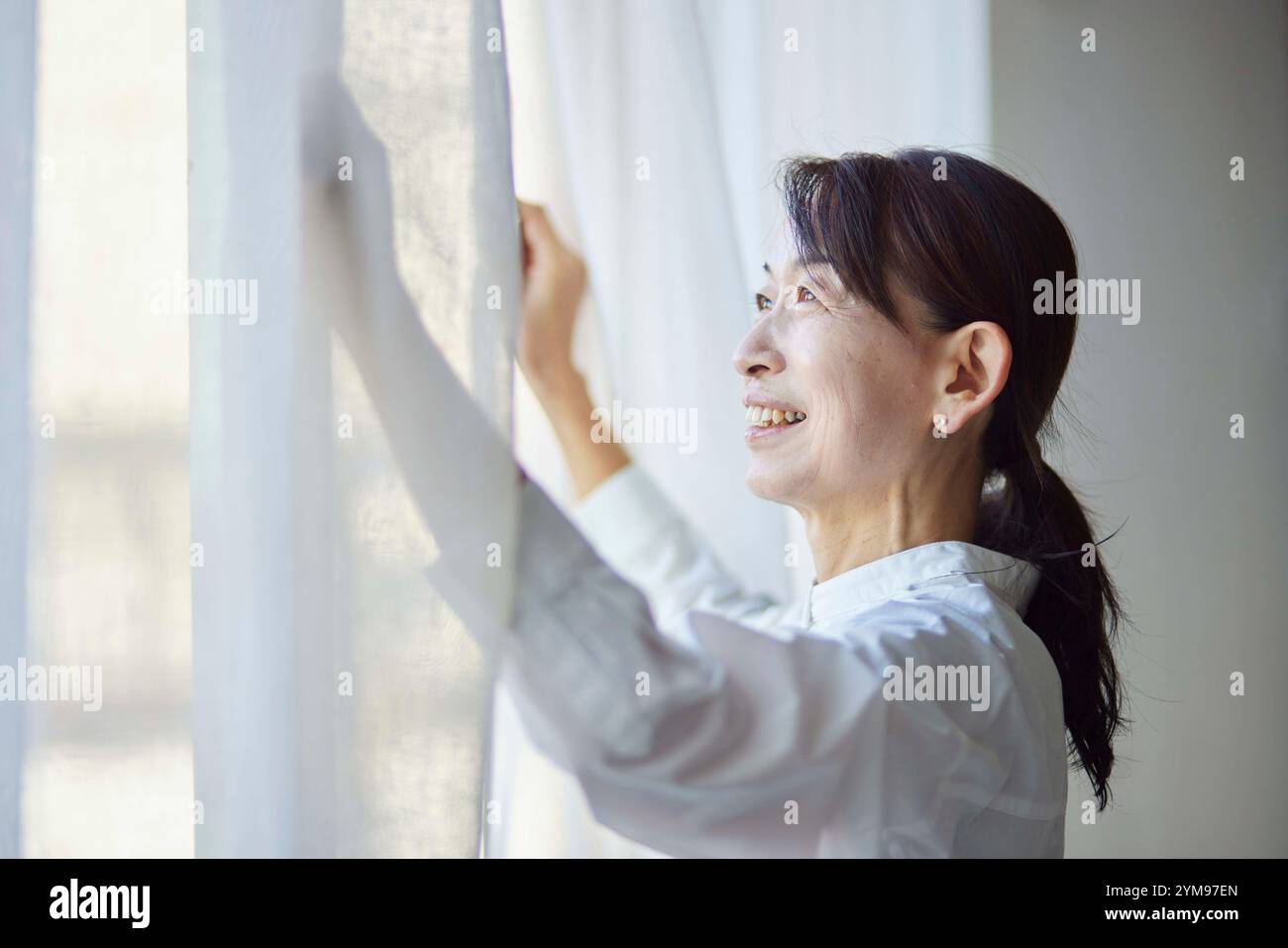 Senior Japanese woman opening the curtains in the living room Stock ...