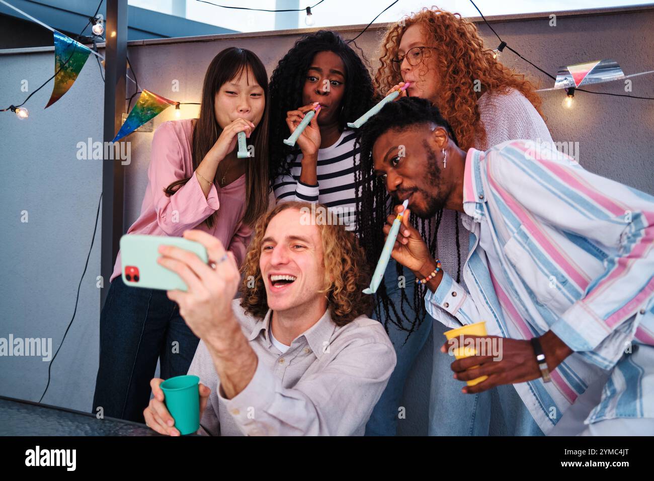 Friends taking a selfie and blowing party horns at rooftop party Stock ...